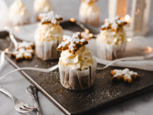 Einfaches Rezept für gewürzte Mandel Cupcakes mit luftigem hellem Orangen-Frischkäsefrosting und heller Zimt-Haselnuss Füllung. Elegant und weihnachtlich dekoriert mit Royal Icing Plätzchen. #Cupcakes #Rezept #Weihnachtscupcakes #Wintercupcakes #Weihnachtstorte #Mürbeteigplätzchen #royalicing