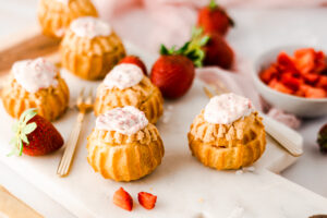 Außen knusprig innen cremig! Diese süßen Mini Windbeutel sind gefüllt mit Vanillepudding und frischen Erdbeerstückchen. Die Choux werden aus Brandteig gemacht, aber keine Sorge, mit diesem Rezept sollte euch auch dieser gelingen! Die Erdbeer Vanille Choux sind perfekt für die Kaffeetafel oder zum Mitnehmen fürs Büro. #Windbeutel #Erdbeeren #Backen #Rezept #Brandteig #Choux