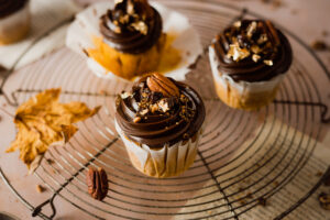 Ein einfaches Rezept für herbstliche Pumpkin Spice Cupcakes mit gebrannten Pekannüssen. Die karamellisierten Nüsse auf einer reichen Schokoadencreme passen einfach so gut zu dem gewürzten saftigen Kürbismuffin! #Pumpkinspice #backen #Rezept #Kürbis #Herbstrezepte #Nüsse #Muffins #Cupcakes