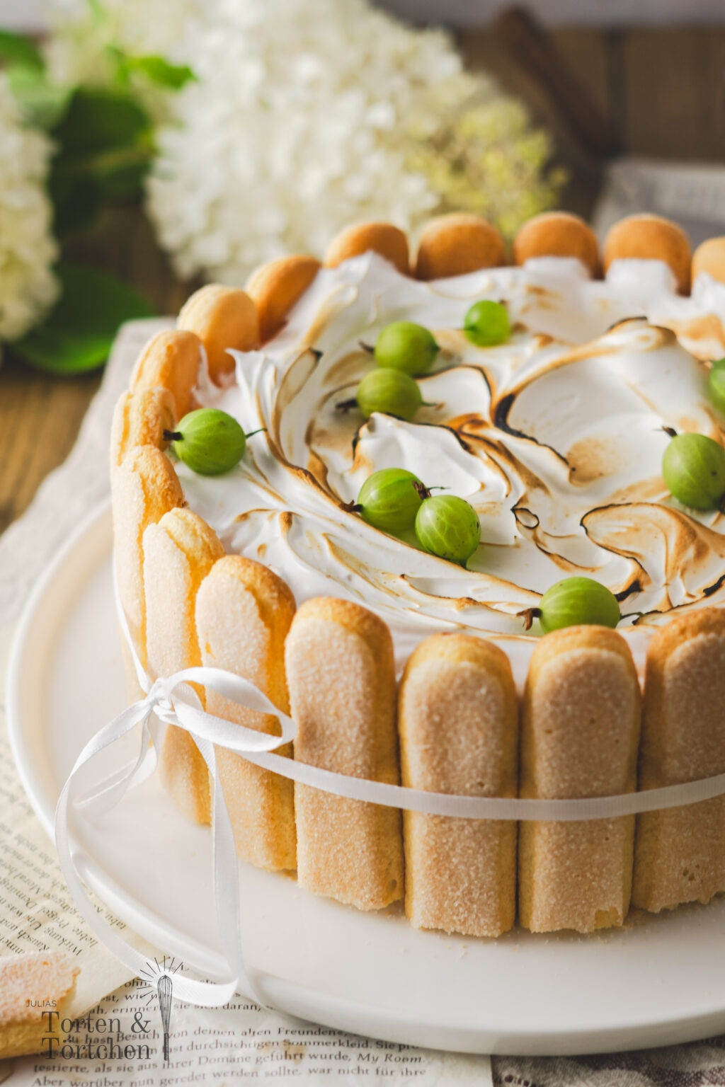 Saisonales Rezept für eine köstliche Stachelbeer-Charlotte mit Baiserhaube. Der saftige Biskuitboden wird mit herber Zitronenlimonade durchtränkt und umhüllt eine fruchtige Stachelbeerfüllung. Eine luftige Baiserhaube, leicht flambiert, verleiht dem Dessert einen besonderen Abschluss. #Stachelbeeren #Stachelbeertorte #Baiser #Rezept #Torte