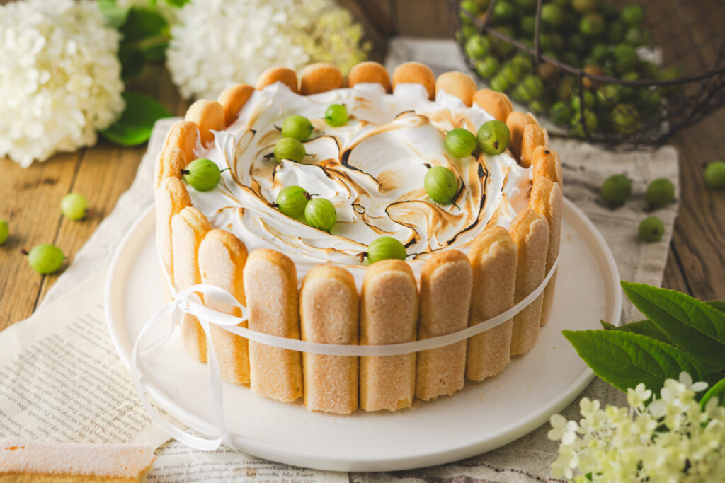 Saisonales Rezept für eine köstliche Stachelbeer-Charlotte mit Baiserhaube. Der saftige Biskuitboden wird mit herber Zitronenlimonade durchtränkt und umhüllt eine fruchtige Stachelbeerfüllung. Eine luftige Baiserhaube, leicht flambiert, verleiht dem Dessert einen besonderen Abschluss. #Stachelbeeren #Stachelbeertorte #Baiser #Rezept #Torte