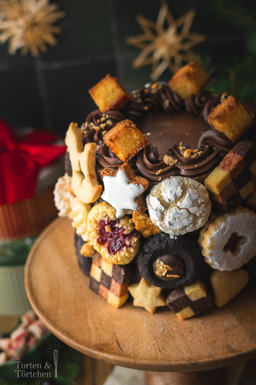 Eine festliche Torte im Germknödel-Stil mit Mohnböden, cremiger Vanillesauce, fruchtigem Pflaumenmus und einer edlen Schokoladenganache. Verziert mit Weihnachtsplätzchen – ideal, um Gäste zu begeistern oder Plätzchenreste kreativ zu verwerten. #Weihnachtstorte #Weihnachtsbäckerei #Backen #Rezept #Weihnachtsplätzchen #Plätzchen