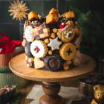 Eine festliche Torte im Germknödel-Stil mit Mohnböden, cremiger Vanillesauce, fruchtigem Pflaumenmus und einer edlen Schokoladenganache. Verziert mit Weihnachtsplätzchen – ideal, um Gäste zu begeistern oder Plätzchenreste kreativ zu verwerten. #Weihnachtstorte #Weihnachtsbäckerei #Backen #Rezept #Weihnachtsplätzchen #Plätzchen