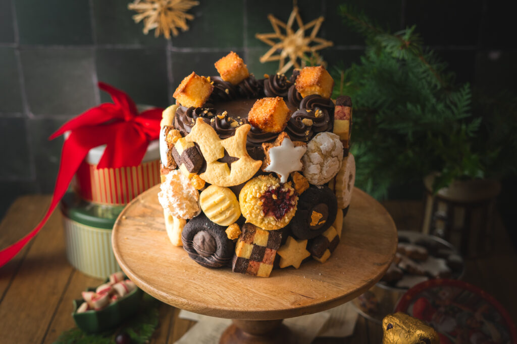 Eine festliche Torte im Germknödel-Stil mit Mohnböden, cremiger Vanillesauce, fruchtigem Pflaumenmus und einer edlen Schokoladenganache. Verziert mit Weihnachtsplätzchen – ideal, um Gäste zu begeistern oder Plätzchenreste kreativ zu verwerten. #Weihnachtstorte #Weihnachtsbäckerei #Backen #Rezept #Weihnachtsplätzchen #Plätzchen